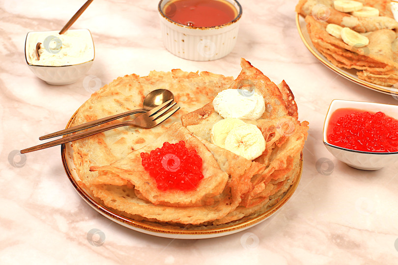 Скачать Вкусные русские блинчики с мягким сыром, бананами, красной икрой и медом на мраморном столе. Полезный завтрак, приготовленный из свежих продуктов, вдохновленный Масленицей и традиционной русской кухней фотосток Ozero