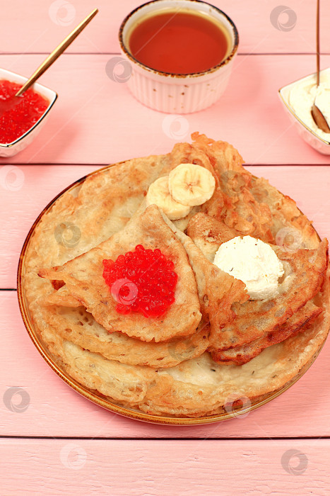 Скачать Вкусные русские блинчики с мягким сыром, бананами и красной икрой на кухонном столе. Полезный завтрак из свежих продуктов, масленичная концепция и традиционная русская кухня, особый акцент фотосток Ozero