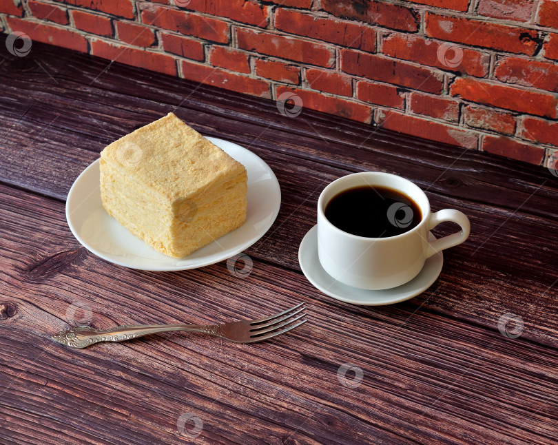 Скачать Кусочек бисквитного торта "Наполеон" на тарелке, вилка и чашка горячего черного кофе на деревянном столе. фотосток Ozero