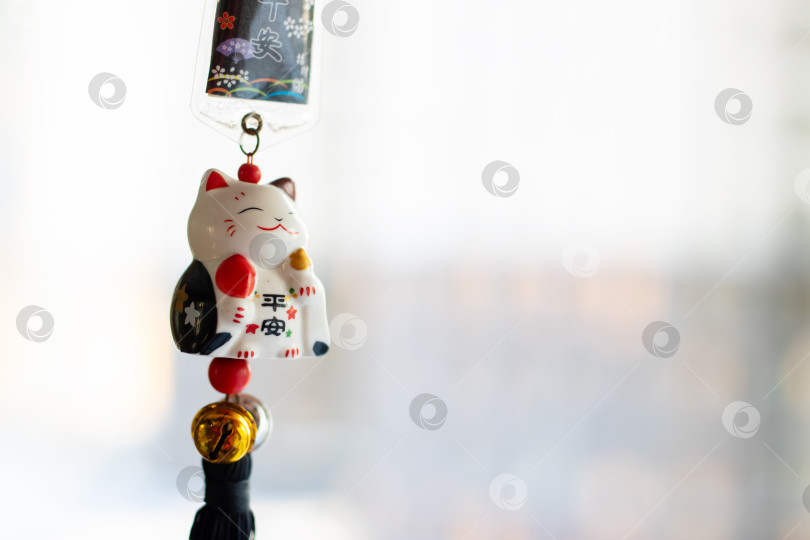 Скачать Подвесной керамический кот-счастливчик с кисточками и монетой создает атмосферу спокойствия в уютной чайной фотосток Ozero