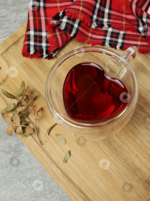 Скачать Уютная чайная чашка в форме сердца рядом с теплым красным пледом на деревянном подносе фотосток Ozero