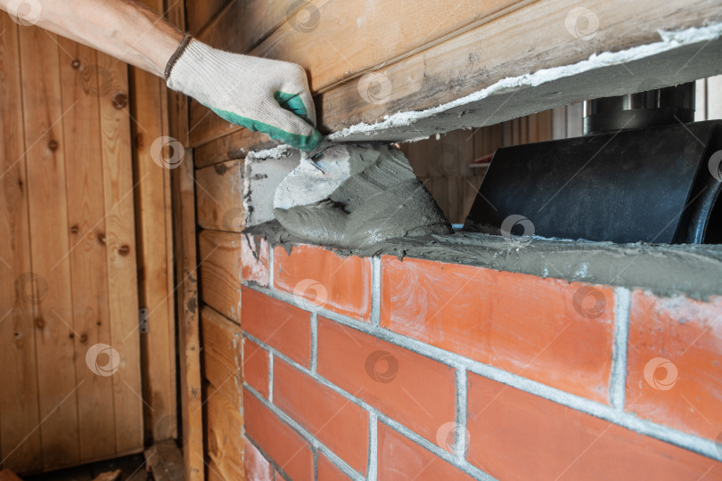 Скачать Каменщик укладывает красный кирпич вокруг банной печи с помощью шпателя. фотосток Ozero
