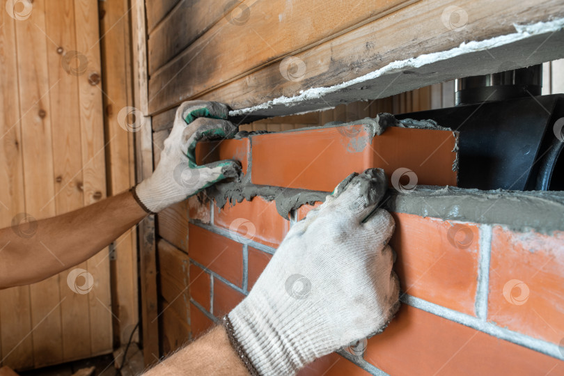 Скачать Каменщик укладывает красный кирпич вокруг печи для бани. Ремонтные работы. фотосток Ozero
