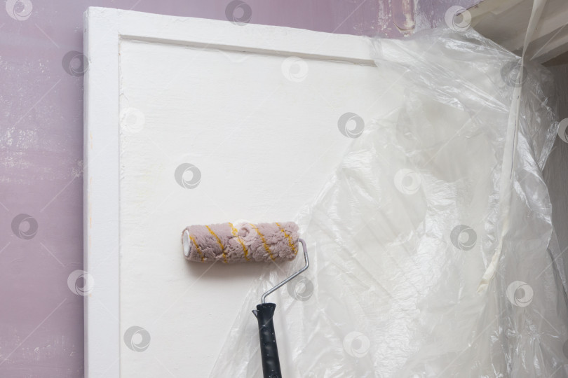 Скачать Валик с длинной ручкой стоит возле белой двери в комнате, стены которой выкрашены в фиолетовый цвет. Ремонт дома или квартиры фотосток Ozero