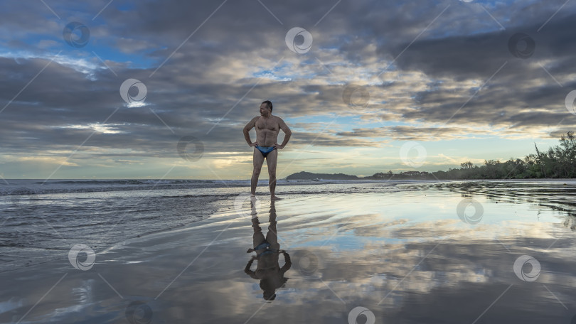 Скачать Мужчина в плавках стоит на берегу океана на рассвете. фотосток Ozero