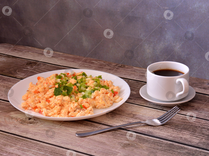 Скачать Яичный омлет, обжаренный с помидорами и украшенный петрушкой, подается на деревянном столе, рядом с ним вилка и чашка черного кофе. фотосток Ozero