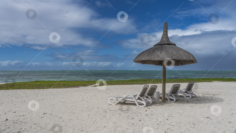 Скачать Ряд шезлонгов на песчаном пляже под соломенным зонтом. фотосток Ozero