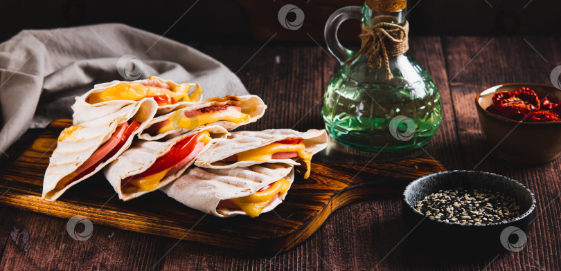 Скачать Бутерброды на гриле с колбасой, сыром и помидорами в тортилье на доске на веб-баннере table фотосток Ozero