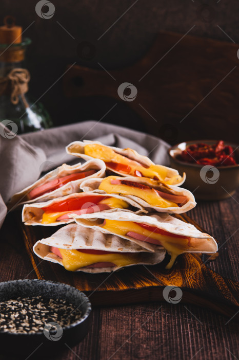 Скачать Приготовленные на гриле бутерброды с колбасой, сыром и помидорами в виде тортильи на доске на столе в вертикальном положении фотосток Ozero