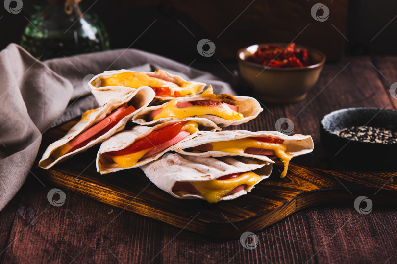 Скачать Приготовленные на гриле бутерброды с колбасой, сыром и помидорами в тортилье на доске на столе фотосток Ozero