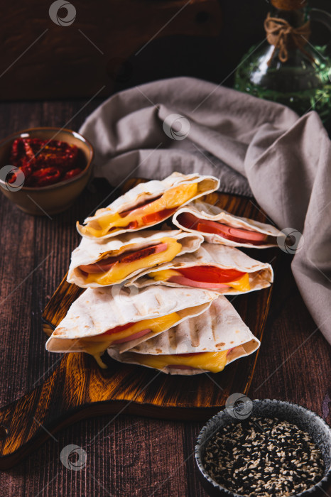 Скачать Колбаса, помидоры и сыр, завернутые в лепешки, приготовленные на гриле, на доске на столе, вид сверху фотосток Ozero