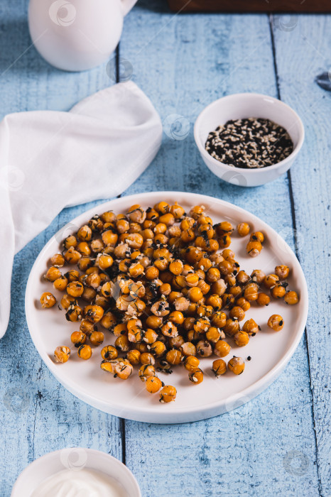 Скачать Аппетитный запеченный нут с кунжутом и зеленью на тарелке на столе, вид сверху фотосток Ozero