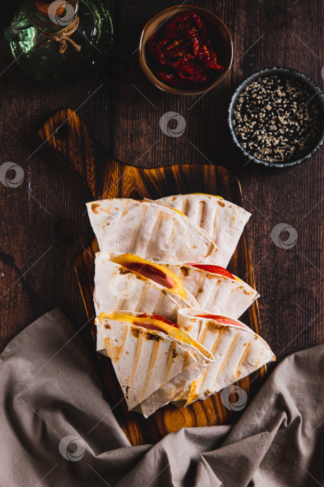 Скачать Колбаса, помидоры и сыр, завернутые в плоские лепешки-гриль, разложенные на доске вертикально фотосток Ozero