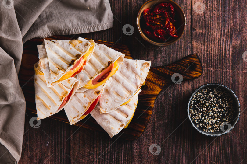 Скачать Приготовленные на гриле бутерброды с колбасой, сыром и помидорами в тортилье на доске, вид сверху фотосток Ozero