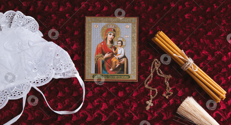 Скачать Икона, крест на цепочке, свечи, шапочка и аспергиллум на фоне красного бархата вид сверху на веб-баннер фотосток Ozero