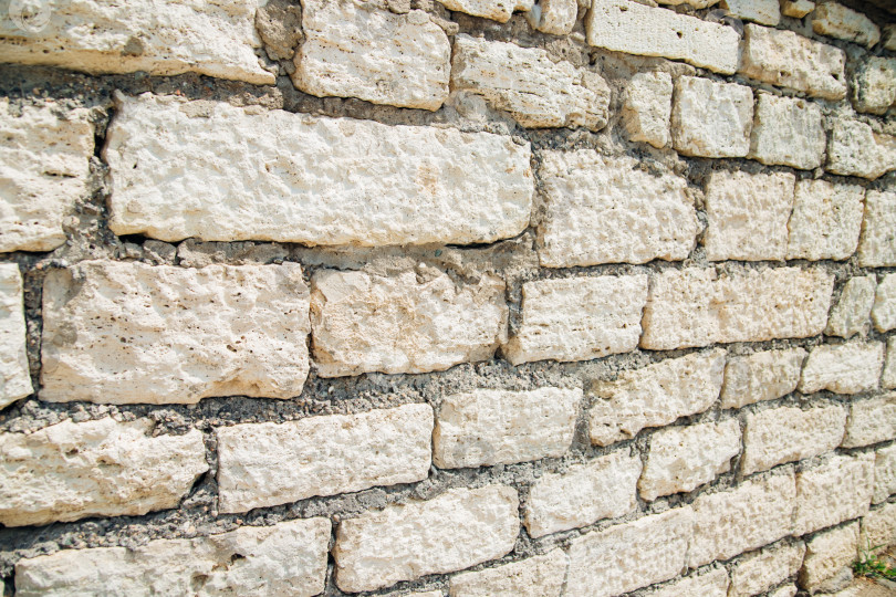 Скачать Текстурированная стена из прямоугольных каменных блоков светло-бежевых оттенков и цемента между ними. фотосток Ozero