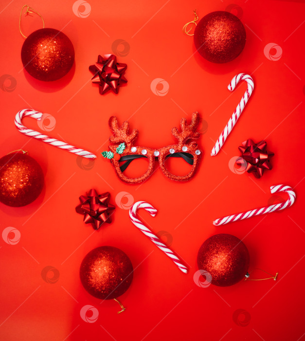 Скачать Новогодние маскарадные очки с оленьими рогами, воздушные шары, леденцы на палочке на красном фоне. Концепция рождественской вечеринки. Веселый праздник. Украшение для детей и взрослых. фотосток Ozero