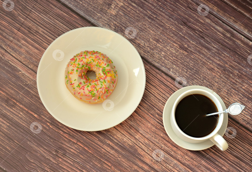 Скачать Свежий пончик с белой ванильной начинкой и топпингом и чашка горячего черного кофе на деревянном столе. фотосток Ozero