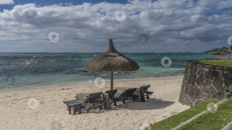 Скачать Ряд шезлонгов под соломенным зонтом на тропическом пляже. фотосток Ozero