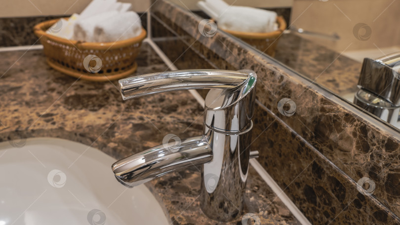 Скачать Блестящий кран из нержавеющей стали на краю белой фарфоровой раковины для умывания. фотосток Ozero