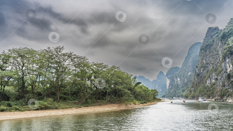 Скачать Живописный речной пейзаж. По руслу реки проплывают туристические суда и бамбуковые плоты. фотосток Ozero