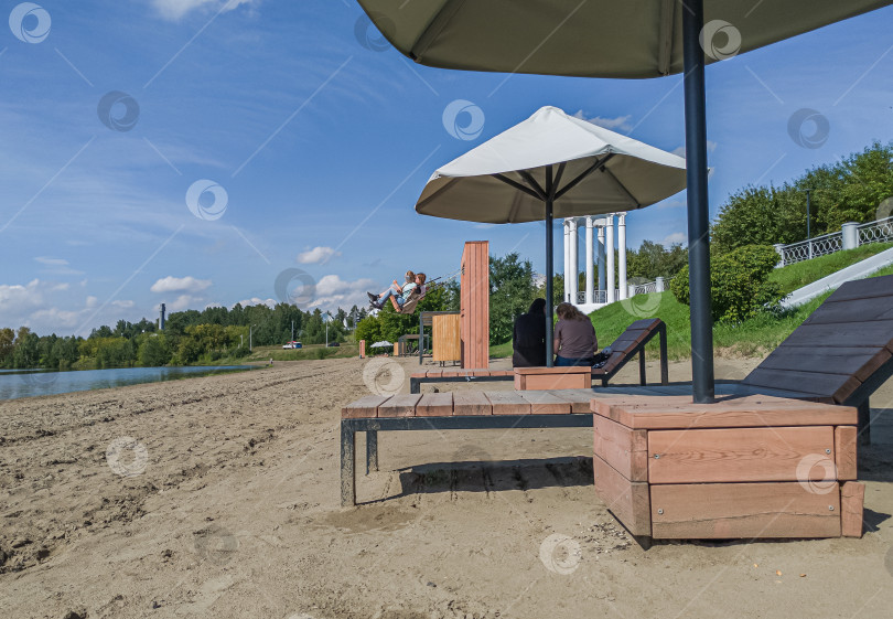 Скачать Россия,город Железногорск Красноярский Край, 08 июля 2025 год. Песчаный берег у воды, зонтик, шезлонги, люди отдыхают. фотосток Ozero