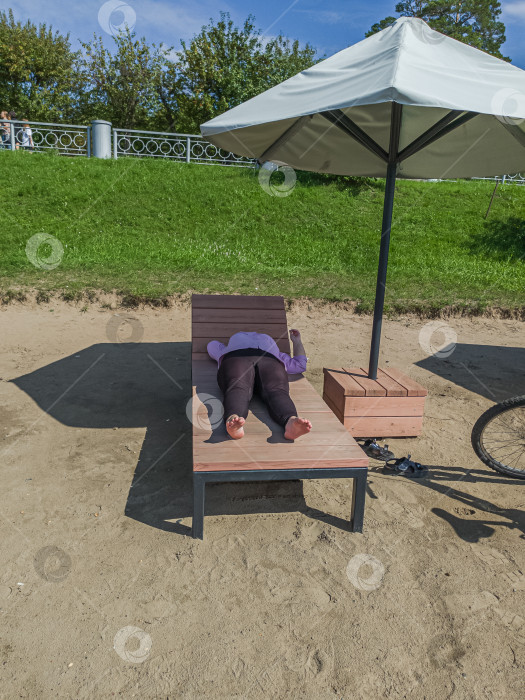 Скачать Россия,город Железногорск Красноярский Край, 08 июля 2025 год. человек лежит на шезлонге под зонтом на песчаной поверхности. фотосток Ozero