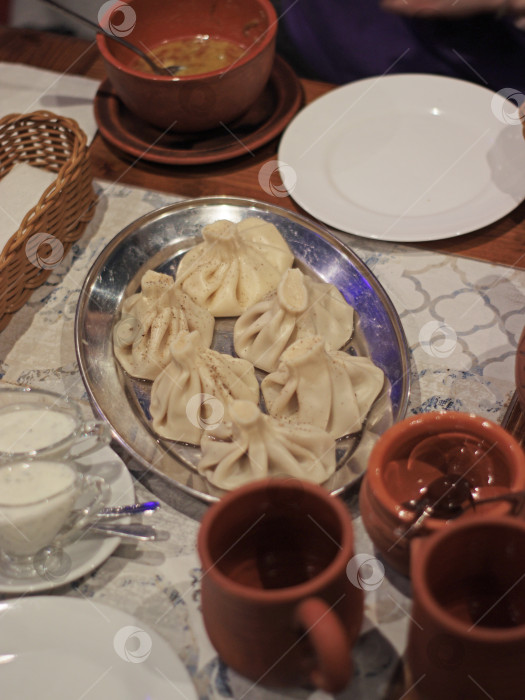 Скачать Традиционные грузинские пельмени хинкали, подаваемые на металлическом подносе с керамическими кружками и мацони, ресторанная сервировка стола, подходящая для меню, кулинарный блог, путеводитель, статья о национальной кухне фотосток Ozero