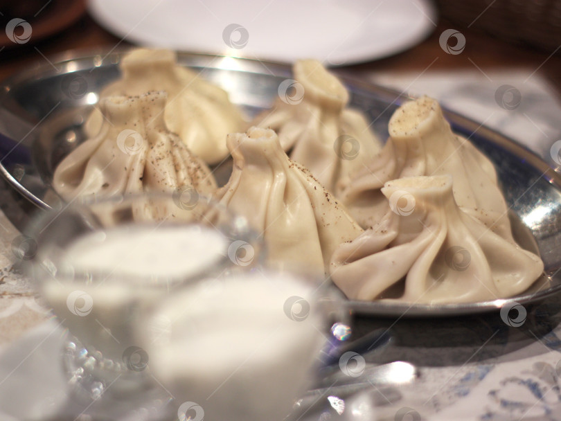 Скачать Пельмени хинкали на металлическом блюде с мацони и черным перцем - аутентичная ресторанная кухня, подходящая для оформления меню, кулинарной статьи, кулинарного блога или публикации о путешествиях. фотосток Ozero