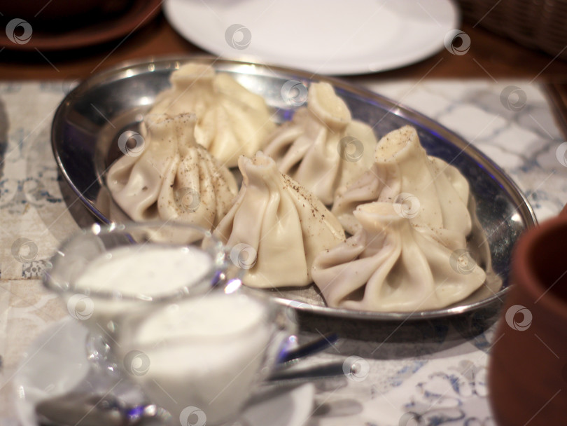 Скачать Пельмени хинкали на металлическом блюде с мацони и черным перцем - аутентичная ресторанная кухня, подходящая для оформления меню, кулинарной статьи, кулинарного блога или публикации о путешествиях. фотосток Ozero