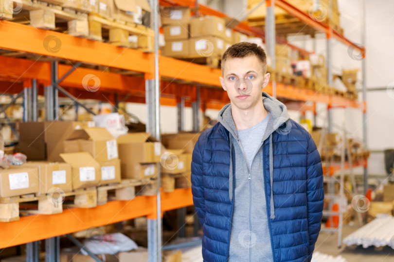 Скачать Молодой человек на логистическом складе с полками и картонными коробками фотосток Ozero