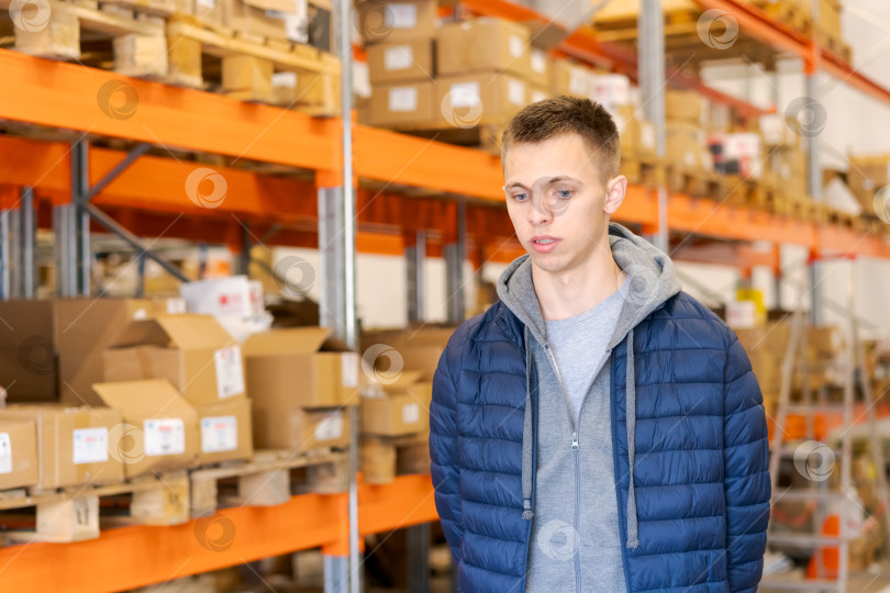 Скачать Молодой человек на логистическом складе с полками и картонными коробками фотосток Ozero