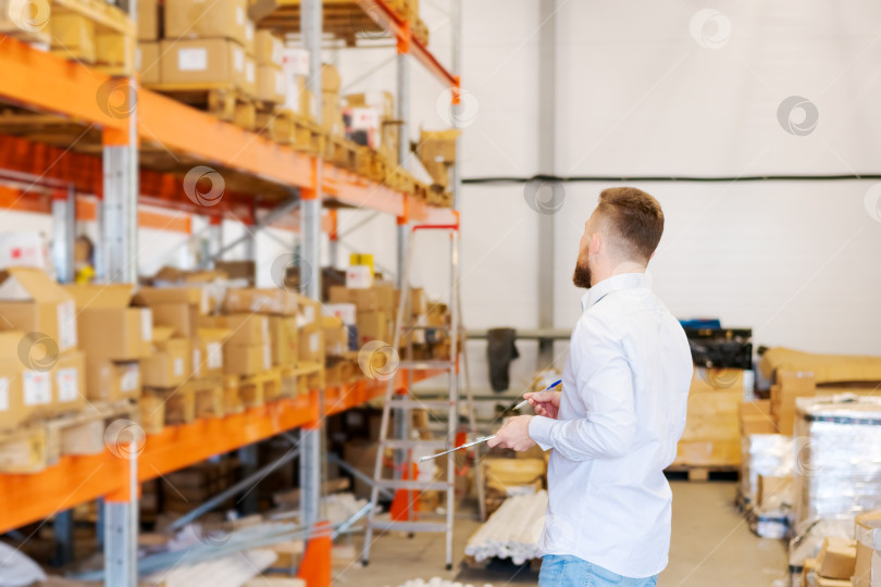 Скачать Мужчина-менеджер по логистике держит в руках буфер обмена во время проверки складских запасов фотосток Ozero