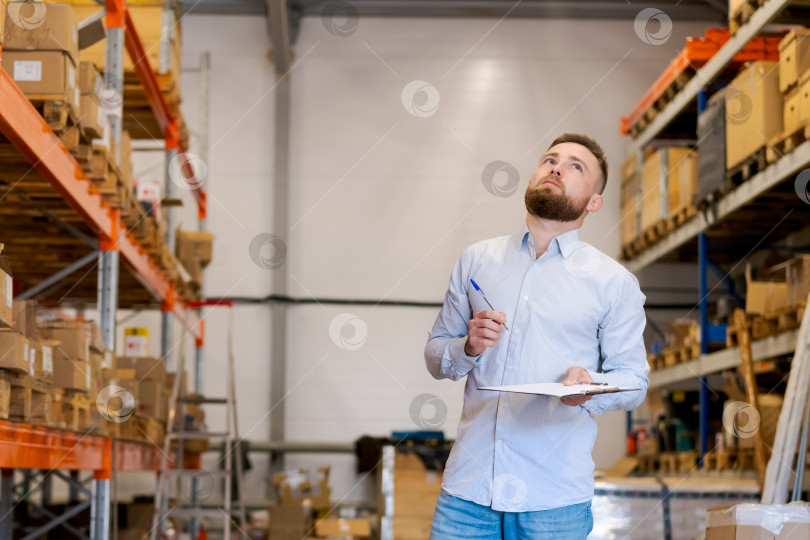 Скачать Менеджер склада смотрит на полки с помощью буфера обмена, планируя запасы и контролируя их фотосток Ozero