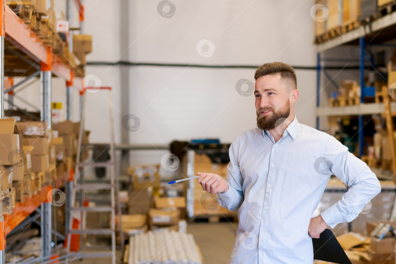 Скачать Уверенный в себе менеджер склада, улыбающийся на фоне лидерства в области складской логистики и операционного успеха фотосток Ozero
