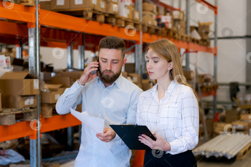 Скачать Менеджер склада разговаривает по телефону с коллегой, просматривающим логистические документы фотосток Ozero