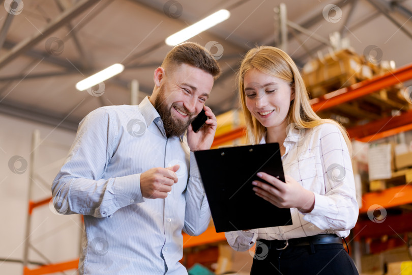 Скачать Счастливые менеджеры по логистике просматривают запасы и разговаривают по смартфонам на складе фотосток Ozero