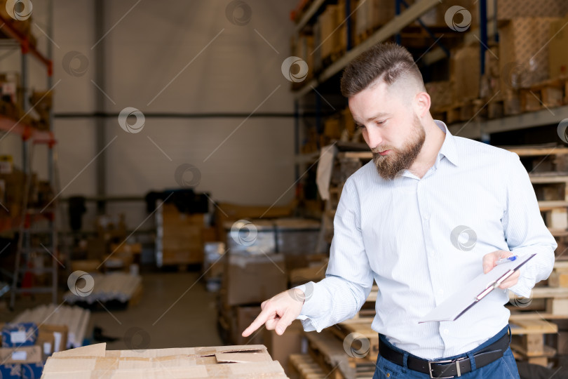 Скачать Сосредоточенный менеджер склада осматривает картонную коробку и держит в руках буфер обмена фотосток Ozero