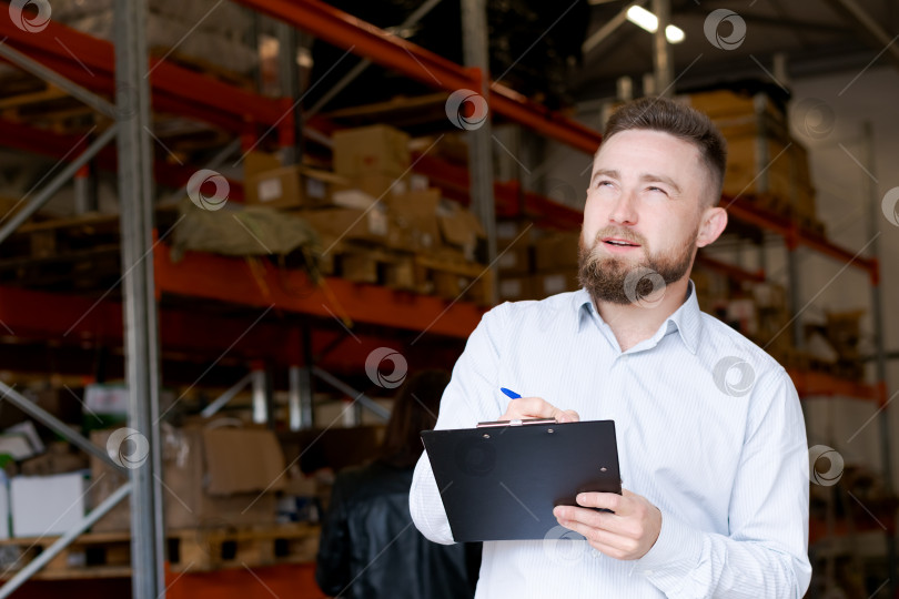 Скачать Сосредоточенный менеджер склада пишет заметки о запасах на фоне складских стеллажей фотосток Ozero