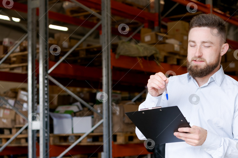 Скачать Менеджер склада пишет заметки об инвентаризации и держит ручку в руках в Распределительном центре фотосток Ozero