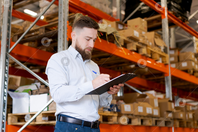 Скачать Сосредоточенный бородатый менеджер склада что-то пишет в планшете обмена на складе фотосток Ozero