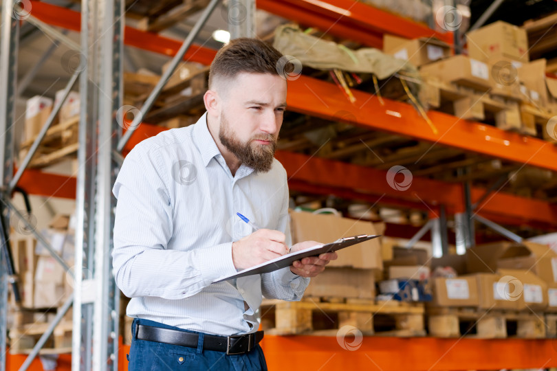 Скачать Сосредоточенный бородатый менеджер склада проводит инвентаризационный аудит с помощью буфера обмена фотосток Ozero