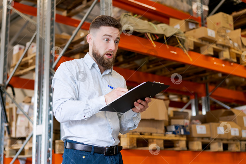 Скачать Удивленный бородатый менеджер склада с буфером обмена во время проверки запасов фотосток Ozero