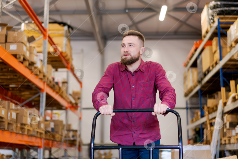 Скачать Улыбающийся менеджер склада с тележкой-платформой в Логистическом центре фотосток Ozero