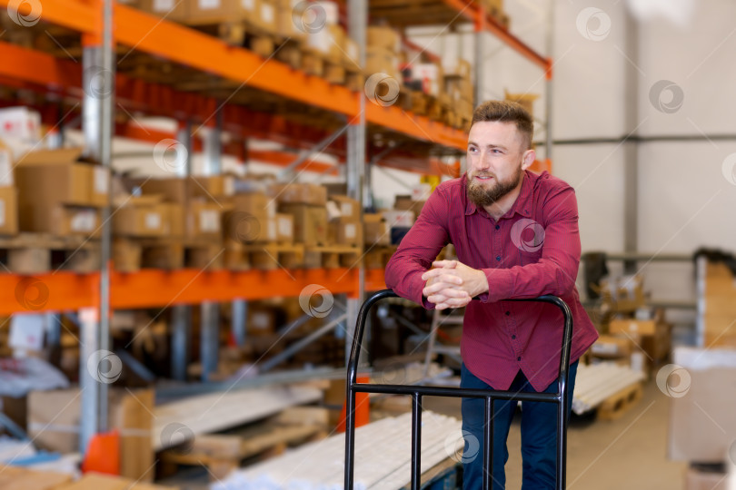 Скачать Уверенный в себе менеджер склада, опирающийся на тележку в логистическом центре фотосток Ozero