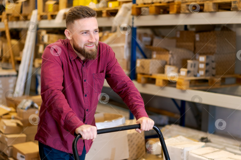 Скачать Улыбающийся сотрудник склада управляет запасами с помощью ручной тележки-платформы фотосток Ozero