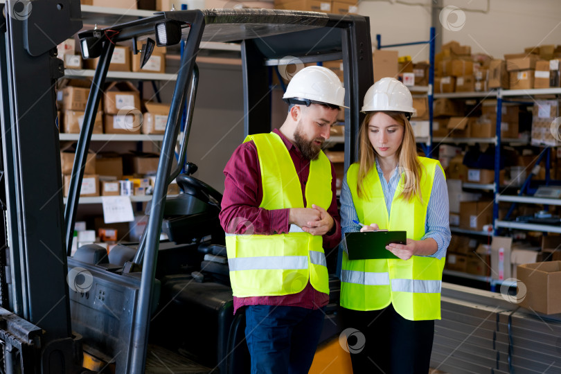 Скачать Менеджеры по логистике в защитном снаряжении обсуждают запасы возле вилочного погрузчика фотосток Ozero