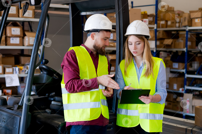 Скачать Менеджеры склада в защитном снаряжении обсуждают запасы возле вилочного погрузчика фотосток Ozero