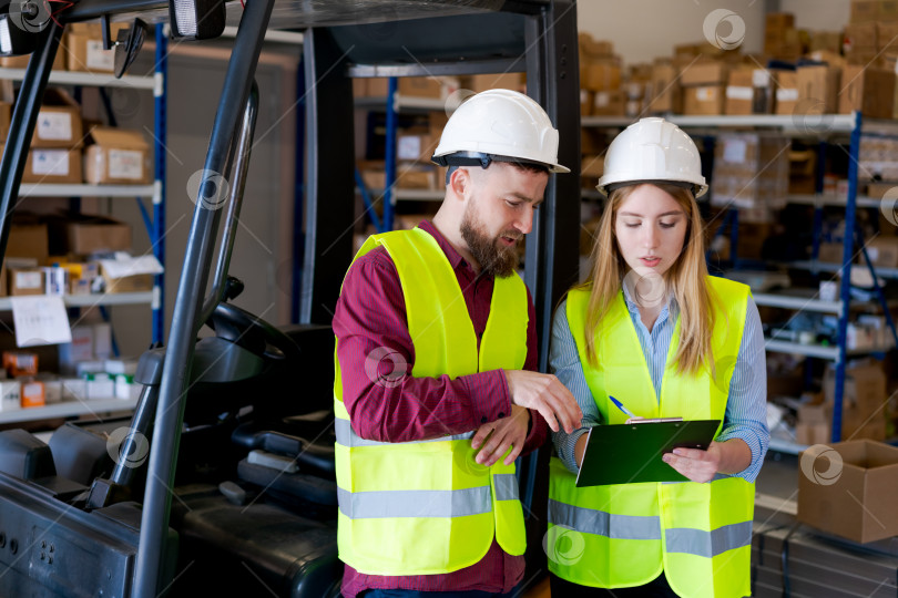 Скачать Команда складской Логистики Координирует Инвентаризацию Запасов Рядом с Вилочным Погрузчиком фотосток Ozero