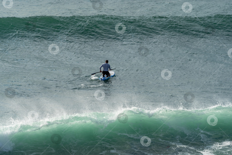 Скачать Спортсмен катается по изумрудной волне Черного моря, накрывающей спортсмена на SUP-доске. Размытый фон. Выборочный фокус. Геленджик, Россия - 19 сентября 2022 г. фотосток Ozero